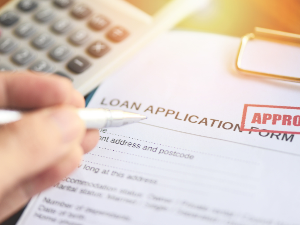 Hand filling out a loan application form marked approved in Australia.