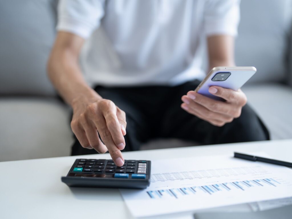 A man holding his phone and clicking numbers on the calculator.